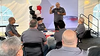 Magna Sterling Heights assembly plant safety program with operators performing ergonomic oil pan loading at stamping workstation, human-centered manufacturing, zero lost-time incident production line, automotive assembly Michigan