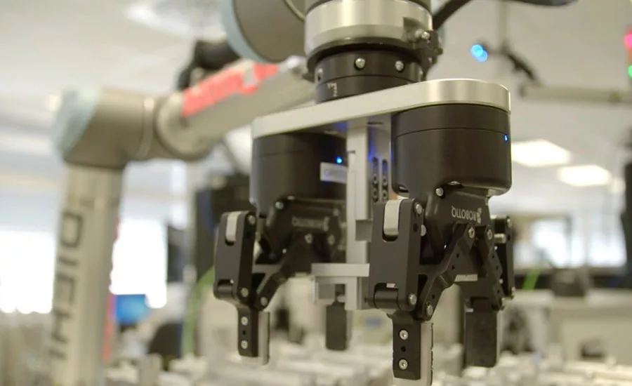 Robotic gripper mounted on a collaborative robot arm in a manufacturing setting.