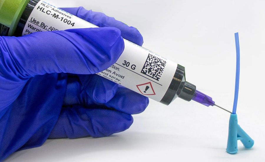 Adhesive being dispensed onto a medical device component.