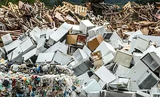 Pile of discarded appliances, scrap metal, wood debris, and plastic waste at a recycling and waste processing facility.