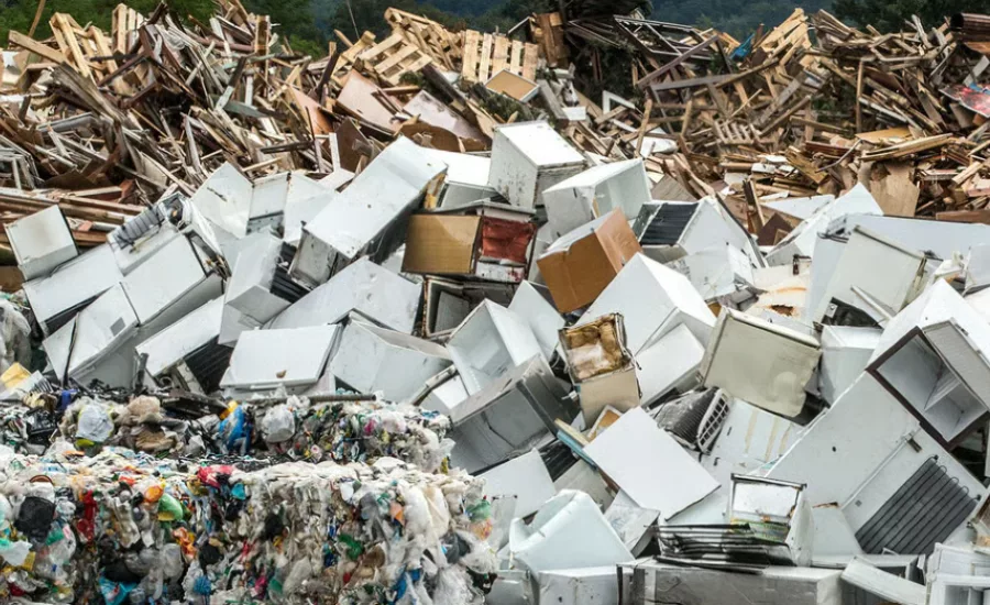 Pile of discarded appliances, scrap metal, wood debris, and plastic waste at a recycling and waste processing facility.