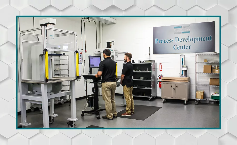 Engineers operating a materials testing system in a process development center, using automated testing equipment to evaluate product performance and manufacturing processes.