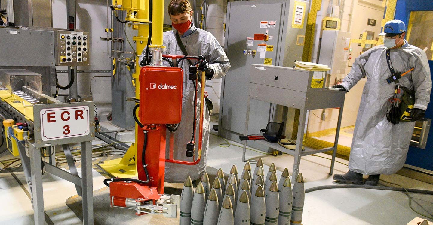 Ordnance technicians use a lift-assist device to aid in the processing of 105-millimeter projectiles