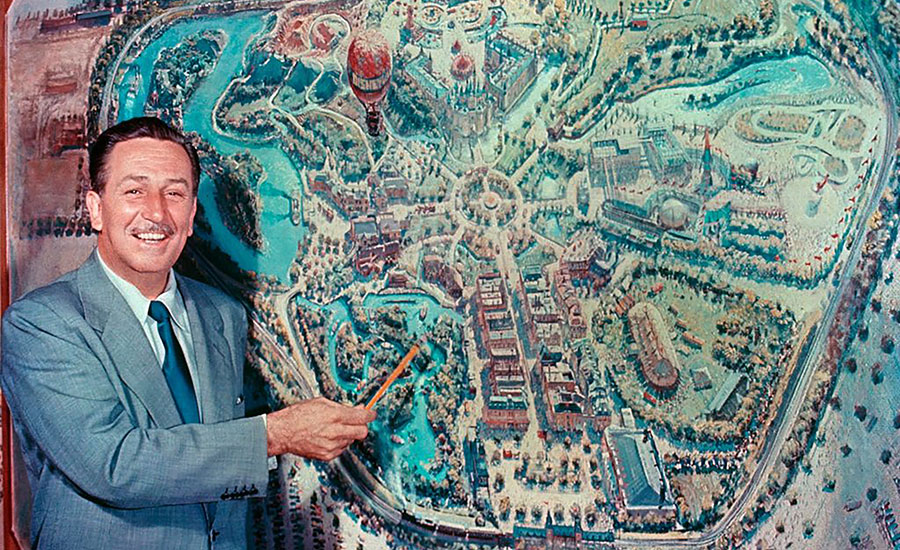Walt Disney in front of a layout of Disneyland